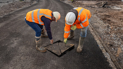 Two construction workers lift a manhole cover in a road using lifting eyes