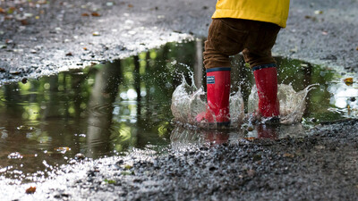 child splashing in a puddle from the rain with welly boots on