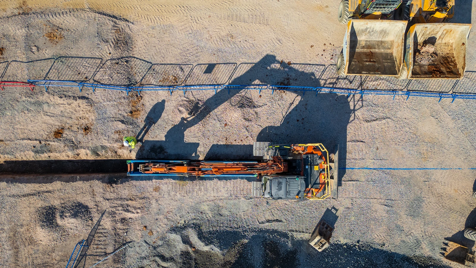 Drone shot of excavator installing deep sewer drainage top down with shadows